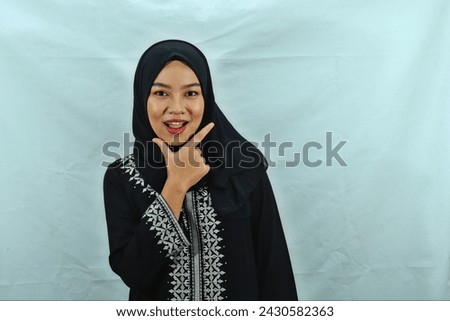Asian Muslim woman wearing hijab, glasses and black dress with white pattern making chis gesture with a satisfied expression isolated on white background Royalty-Free Stock Photo #2430582363