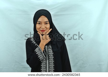 Asian Muslim woman wearing hijab, glasses and black dress with white pattern making chis gesture with a satisfied expression isolated on white background Royalty-Free Stock Photo #2430582365