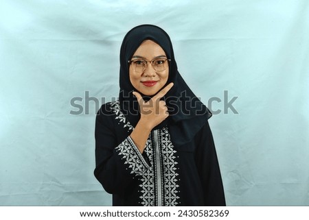 Asian Muslim woman wearing hijab, glasses and black dress with white pattern making chis gesture with a satisfied expression isolated on white background Royalty-Free Stock Photo #2430582369