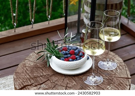 Two glasses of white wine and a plate of wild blueberries and raspberries on a wooden table in a cafe. High angle view. Royalty-Free Stock Photo #2430582903