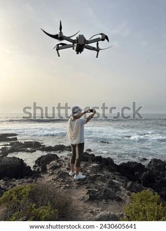 Rear view of senior woman on a rocky beach taking pictures of the ocean waves, a drone device flights above the lady.  Concept of relaxed elderly person admiring the power of nature