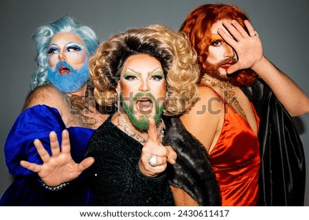 Group of drag queens in elegant outfits, standing together and striking poses of outrage, panic and confusion and ponting a finger at camera