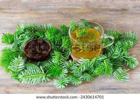 a drink made of pine needles in a cup with green fir needles and pine cone jam on a wooden table close-up Royalty-Free Stock Photo #2430614701