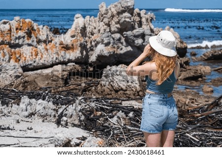 Woman standing taking a photo of the ocean with a smart phone