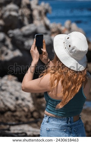 Woman standing taking a photo of the ocean with a smart phone