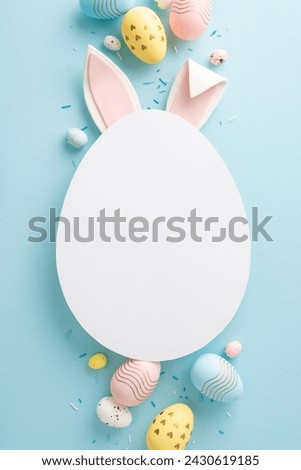 Picture-perfect Easter setup: vertical top view of vibrant eggs, sprinkles and rabbit ears emerge from an egg-shaped cutout on a pastel blue background, inviting personalized greetings or ads