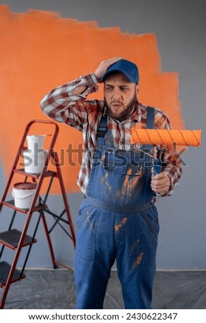 Painter man holding a paint roller on wall background with headache and problem on the workplace. Copy space