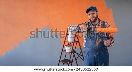 Young painter caucasian man holding roller on orange wall background showing thumb down with negative expression. Banner. Copy space
