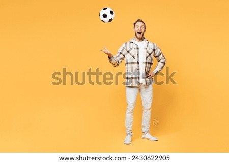 Full body happy young man fan wears brown shirt casual clothes cheer up support football sport team hold toss up soccer ball watch tv live stream look aside on area isolated on plain yellow background