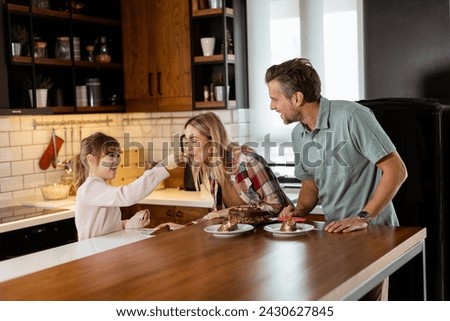A heartwarming scene unfolds as a family relishes a mouthwatering chocolate cake together in the warmth of their sunlit kitchen, sharing smiles and creating memories Royalty-Free Stock Photo #2430627845