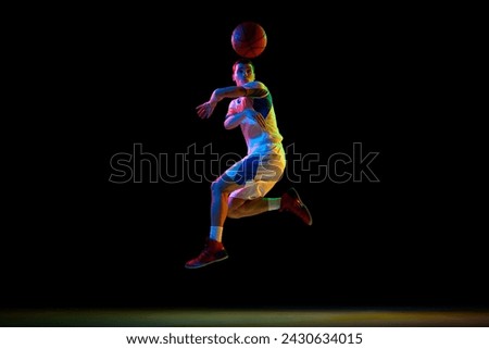 Action photo of young athlete man, basketball player doing pass against black studio background in mixed neon light. Concept of professional sport, energy, strength and power, match, championship.