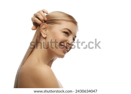 Side profile view photo of smiling woman holding her ponytail against white studio background. Hairstyles and hair care treatments. Concept of natural beauty, anti aging, cosmetology, female health.