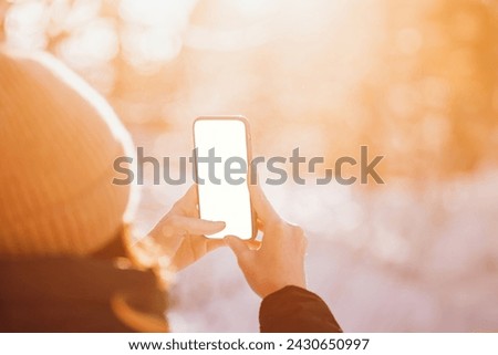 Smartphone mockup in womans hand. She is in a park in winter and enjoys nature photography.