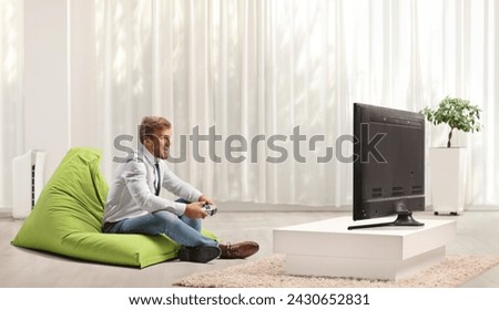 Businessman on a beanbag armchair playing football video game with joystick at home