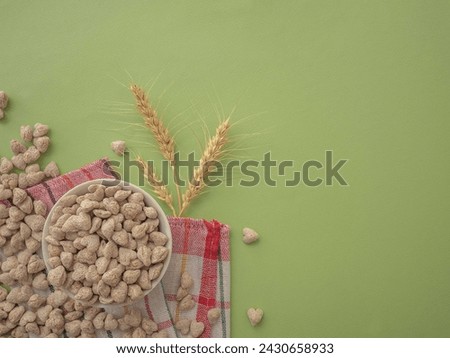 Extruded heart-shaped bran in a white plate on a green background, kitchen napkin with red stripes. Spikelets of wheat. The layout for the label. A place for the text.