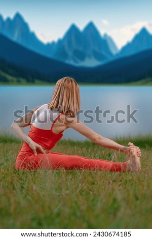 Relaxed young yoga woman stretching body near lake in mountains, Perfect symmetry: Young woman's yoga pose aligns with the beauty of a mountain lake