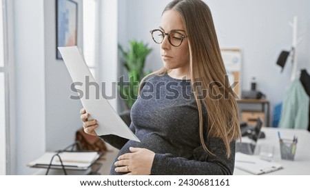 A pregnant hispanic woman reads a document in an office, portraying maternity in the workplace. Royalty-Free Stock Photo #2430681161
