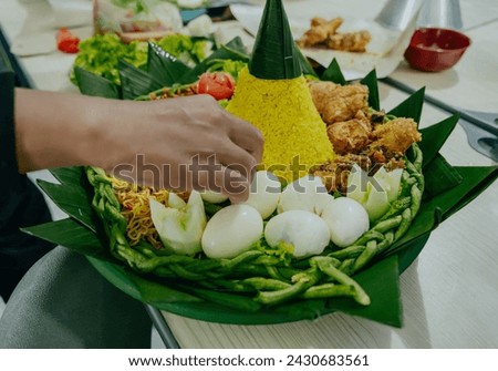 Process of decorating yellow rice in a cone shape. In Indonesia called "Nasi Tumpeng" A festive Indonesian rice dish with side dishes. Tumpeng rice in green plastic tray.  Royalty-Free Stock Photo #2430683561