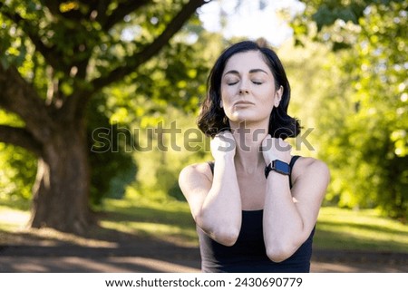 Close-up photo of young tired woman doing sports and exercising outdoors, standing exhausted with closed eyes, holding hands on neck, doing massage and resting.