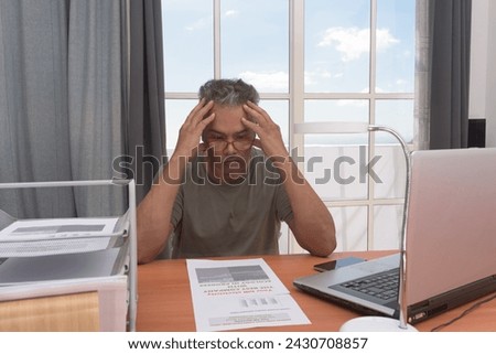 Mature man sits with laptop, paperwork, addressing electricity bill conflict, he is anger,depicting responsibility and problem-solving in modern life,hands on forehead,there's blue sky behind him Royalty-Free Stock Photo #2430708857