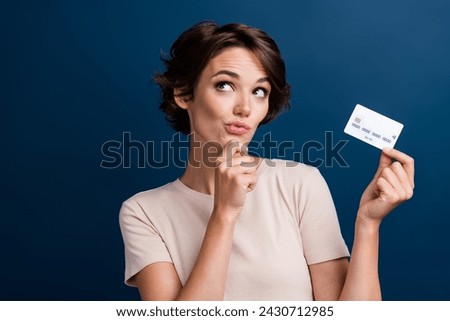 Photo portrait of lovely lady hold credit card look minded empty space dressed stylish white garment isolated on dark blue color background