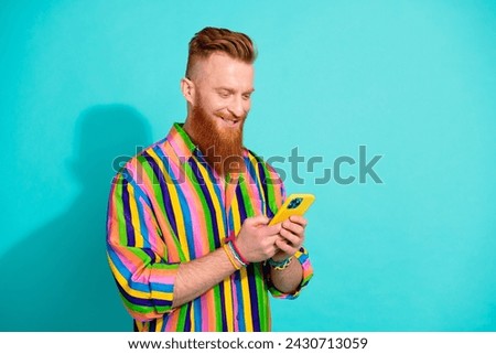 Photo of cheerful irish bearded guy surfing news feed in smartphone click like and repost button isolated on cyan color background
