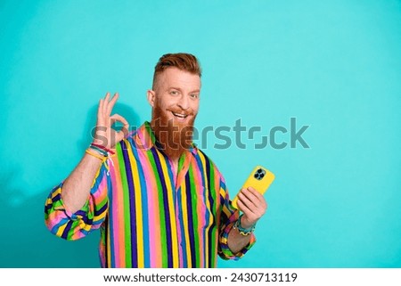 Photo of handsome cheerful guy show okey symbol recommendation using mobile app for smartphone isolated on aquamarine color background