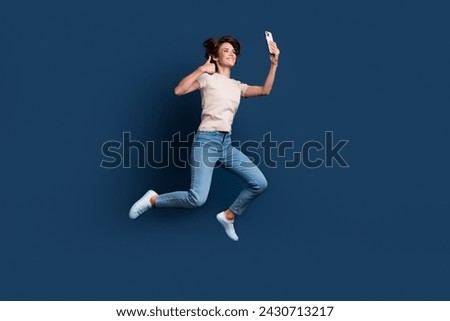 Full size photo of attractive young woman jump run selfie device thumb up wear trendy white clothes isolated on dark blue color background