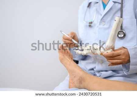 An orthopedic doctor holding a model of ankle and foot bones is explaining to a patient foot bone problems. Concept of health care for feet and foot bones