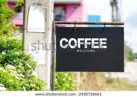 A black sign that says COFFEE WELCOME in white letters, hanging off a rusty pole.