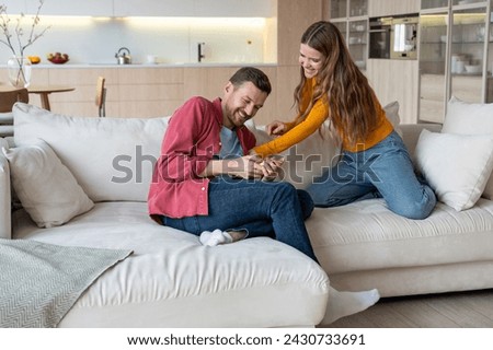 Cheerful girlfriend tickling laughing sensitive boyfriend at home. Loving couple spending lazy weekend, amusing, playing, enjoy every moment. Sincere vivacious positive feelings, harmony in relations. Royalty-Free Stock Photo #2430733691