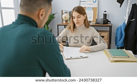 Man and woman discuss documents in a modern office setting, depicting teamwork and professional collaboration. Royalty-Free Stock Photo #2430738327