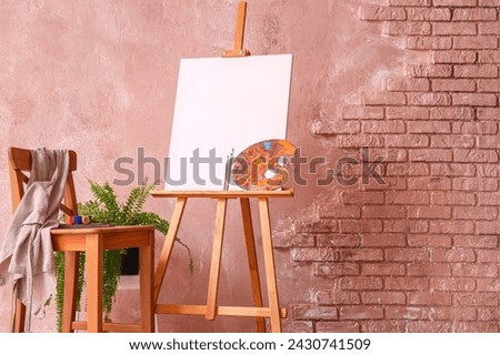 Wooden easel with blank canvas and painting tools near color wall in artist's workshop