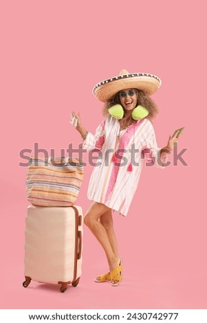 Mature woman in sombrero hat with passport and suitcase on pink background. Mexico's Day of the Dead (El Dia de Muertos) celebration Royalty-Free Stock Photo #2430742977