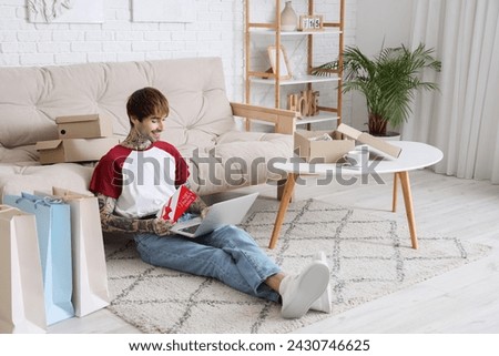 Young tattooed man with laptop and gift voucher shopping online at home