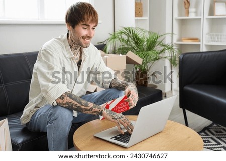 Young tattooed man with gift voucher and laptop shopping online at home