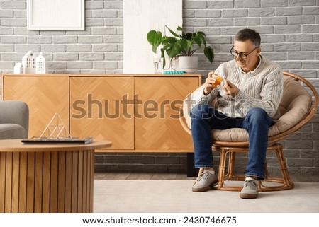 Middle-aged man taking pills from pill bottle at home Royalty-Free Stock Photo #2430746675