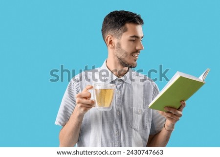 Young man with cup of tea and book on blue background