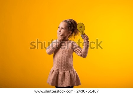 Portrait of thoughtful child girl holding paper bulb and pointing finger up. Success, motivation, winner, genius, idea concept
