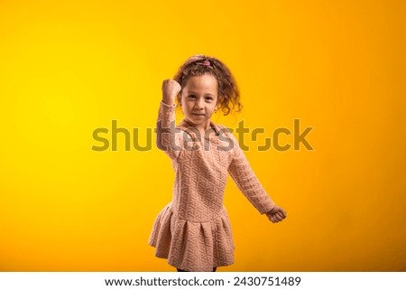 Portrait of enraged Child girl showing fist at camera on yellow background. Negative emotions concept Royalty-Free Stock Photo #2430751489