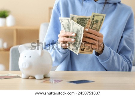 Woman with piggy bank and credit cards counting money at home