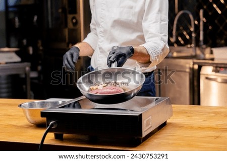 close-up of chef holding a frying pan with a piece of pink duck breast with rosemary over the stove