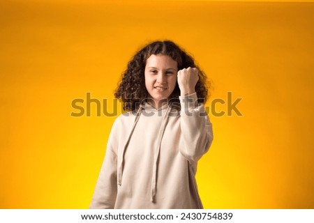 Portrait of enraged girl showing fist at camera on yellow background. Negative emotions concept Royalty-Free Stock Photo #2430754839