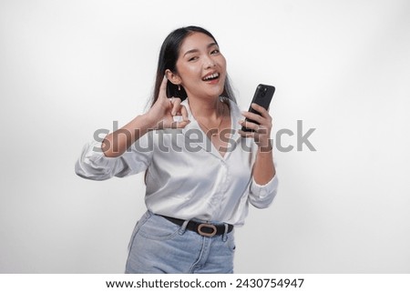 Cheerful Asian woman proudly showing little finger dipped in purple ink after voting for president and parliament election while left hand holding phone, expressing excitement and happiness Royalty-Free Stock Photo #2430754947