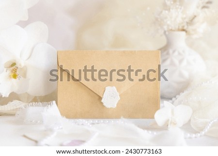 Sealed envelope near white orchid flowers and decor close up,  mockup. Pastel romantic scene with horizontal blank card for Wedding, Valentines, Spring or Mothers day stationery