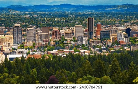 Aerial view of Portland, Oregon, showcasing urban skyline against forested hills. Photographed from Pittock Mansion viewpoint.