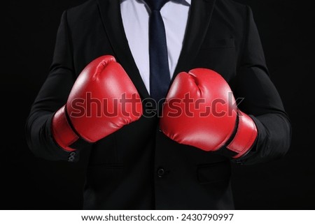 Businessman in suit wearing boxing gloves on black background, closeup