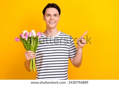 Photo of preppy student dressed striped t-shirt hold bouquet of flowers indicating at sale empty space isolated on yellow color background