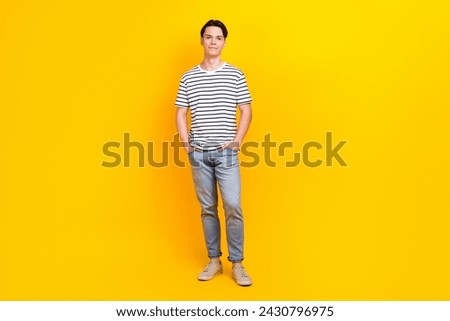 Full size photo of good mood student dressed striped t-shirt jeans trousers keep palms in pockets isolated on yellow color background