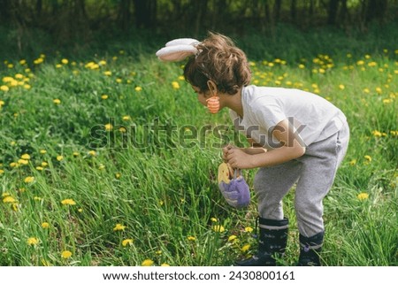 Funny boy with eggs basket and bunny ears on Easter egg hunt in sunny spring garden. Hunting for Easter eggs